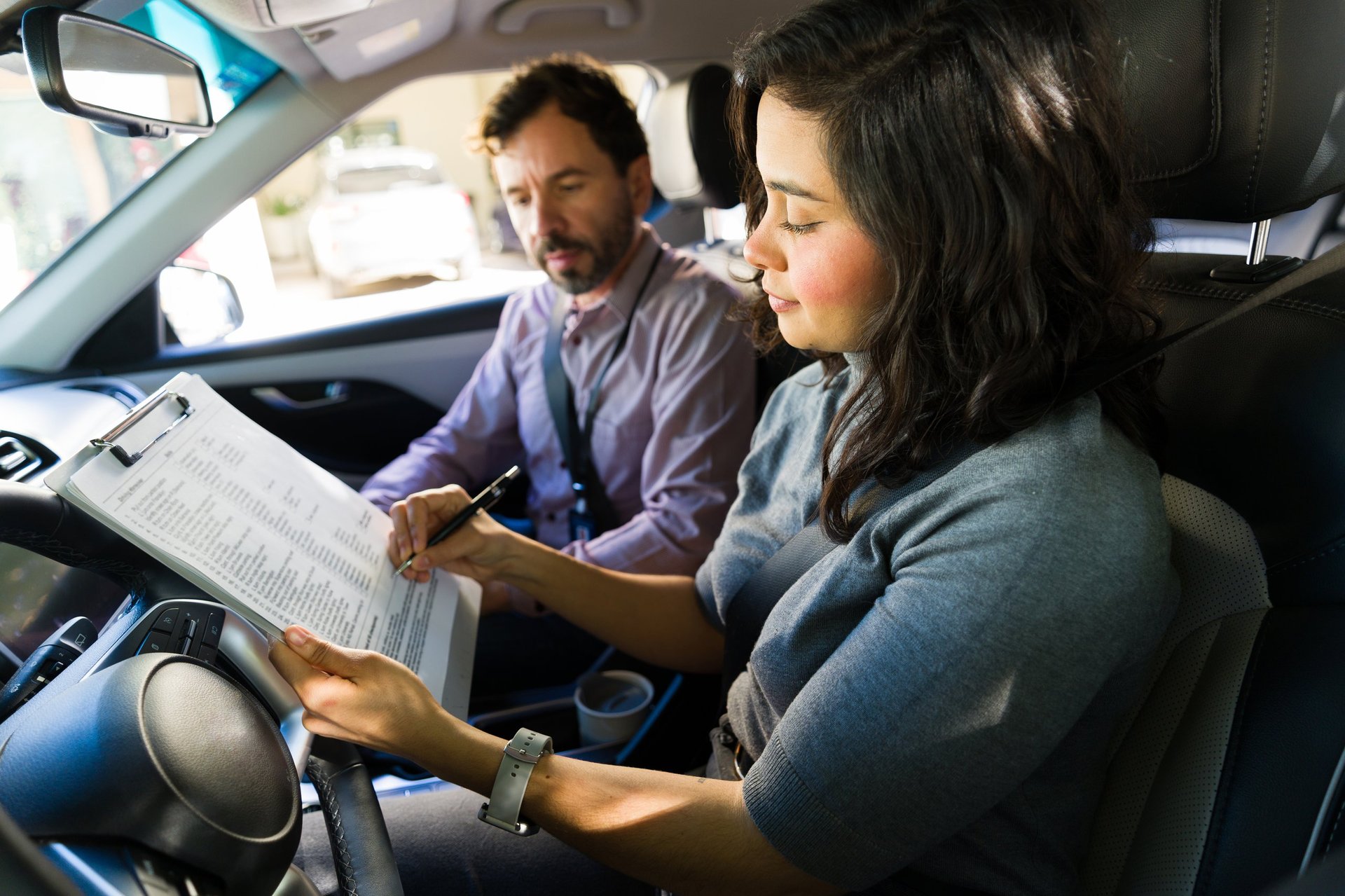 Female student getting ready for a road test, going over a checklist for her driver's license with her male driving instructor in a vehicle