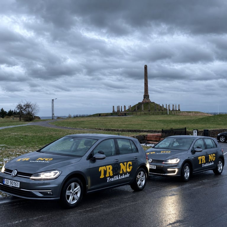 Two dark tour vehicles parked on a road with a stone monument and green hillside under cloudy sky in background